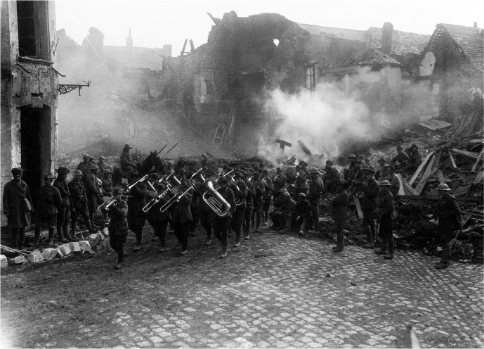 Source 16.7 The band of the Australian 5th Brigade marches through Bapaume on 19 March 1917, while the town is still burning after the German withdrawal [AWM/E00426].